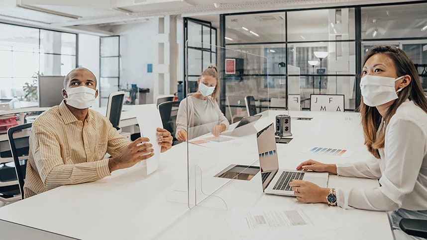 A man and two women wearing face coverings while working at an office conference table