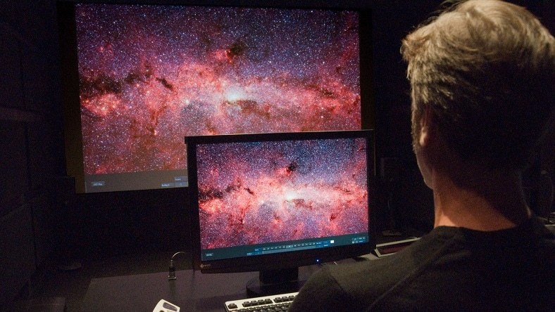 Man viewing VFX shot of a galaxy on computer screens.