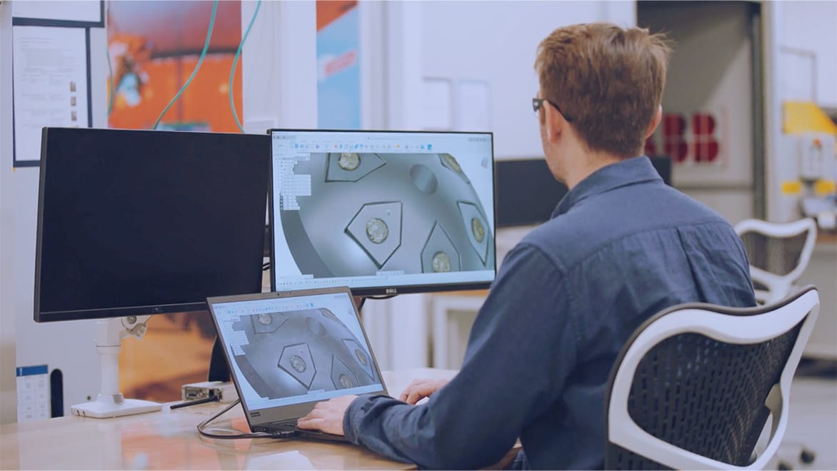 A man sitting at desk looking at computer screens trying to design coral skeleton mold using Autodesk Fusion 360.